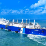 A large blue and white Summit Group liquefied natural gas (LNG) tanker sails on calm, turquoise waters under a bright sky, equipped with advanced processing structures and pipes to deliver locked-in fuel at market price.