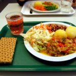 A school lunch on a green tray with vegetables, potatoes and a drink
