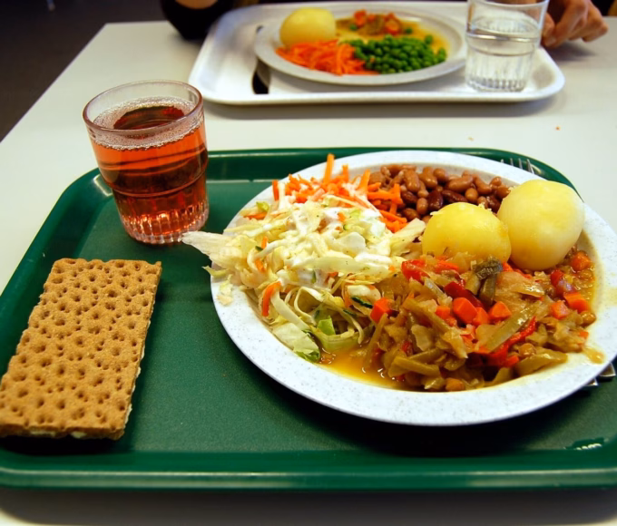A school lunch on a green tray with vegetables, potatoes and a drink