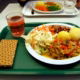 A school lunch on a green tray with vegetables, potatoes and a drink