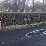A pothole marked out in white paint beside a traffic cone