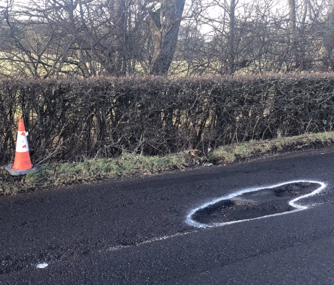 A pothole marked out in white paint beside a traffic cone