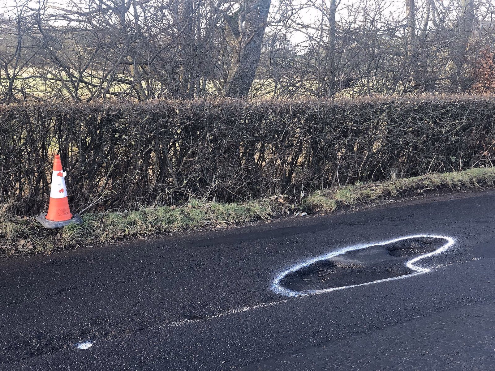 A pothole marked out in white paint beside a traffic cone